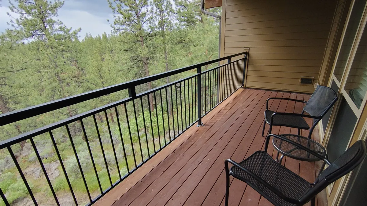 This image features the corner of a balcony with two chairs facing each other, wooden flooring, and trees all around. The cozy arrangement and lush backdrop make it easy to imagine enjoying a coffee, a book, or an intimate conversation while immersed in nature.