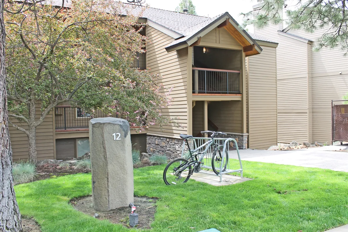 This exterior scene features a stone marker with the number 12, a bike rack, and a landscaped green area. The area looks ready for active use, with space for bikes and a welcoming communal vibe enhanced by the greenery.