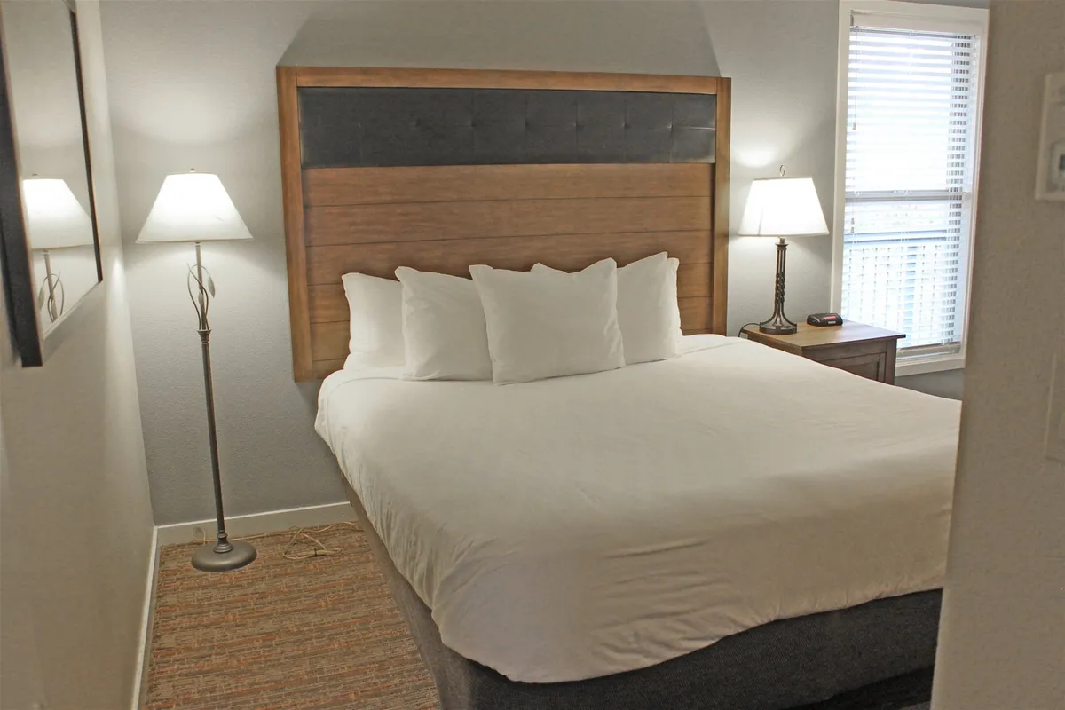 A bright, comfortable bedroom with a welcoming bed, bedside lamps, and a window letting in natural light. The inviting setting encourages relaxation, reading, or enjoying a peaceful morning coffee in bed.