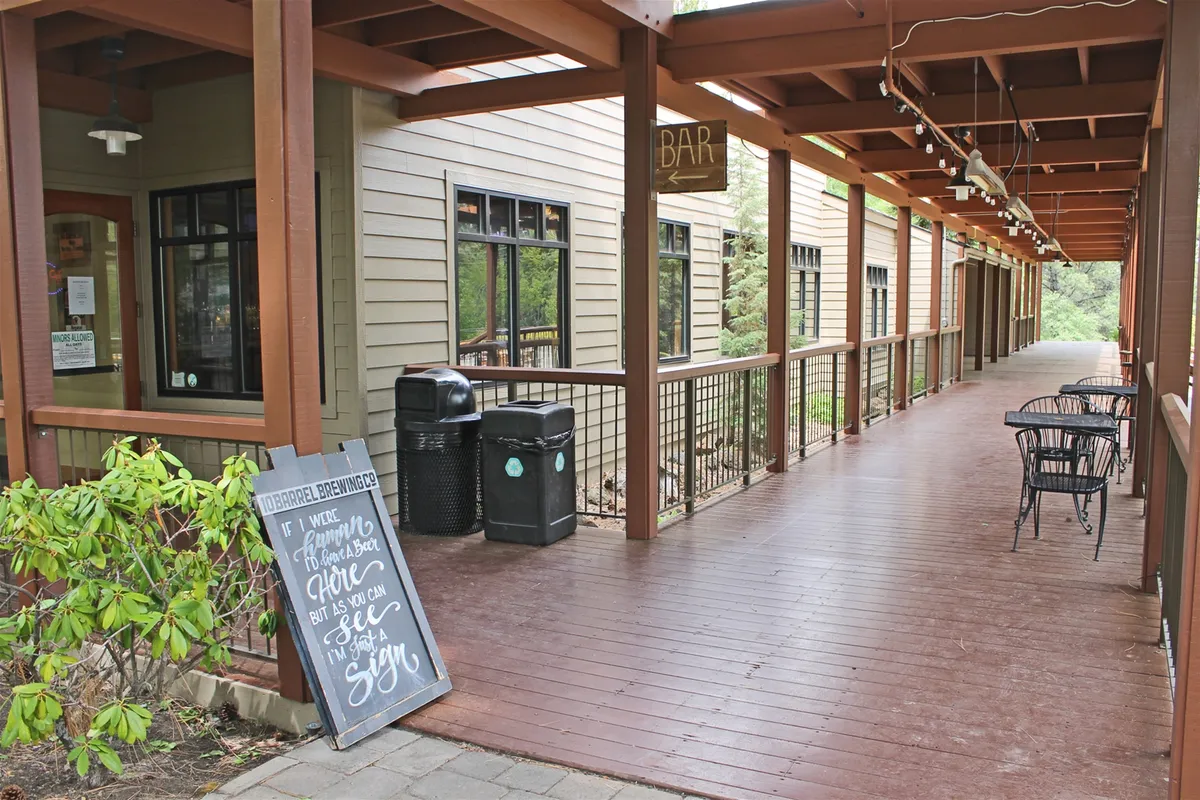 An inviting exterior bar area with a prominent bar sign, chalkboard menu, wooden deck, and comfortable black chairs. The space is casual and social, perfect for enjoying an on-site meal or drink after a day of adventure.