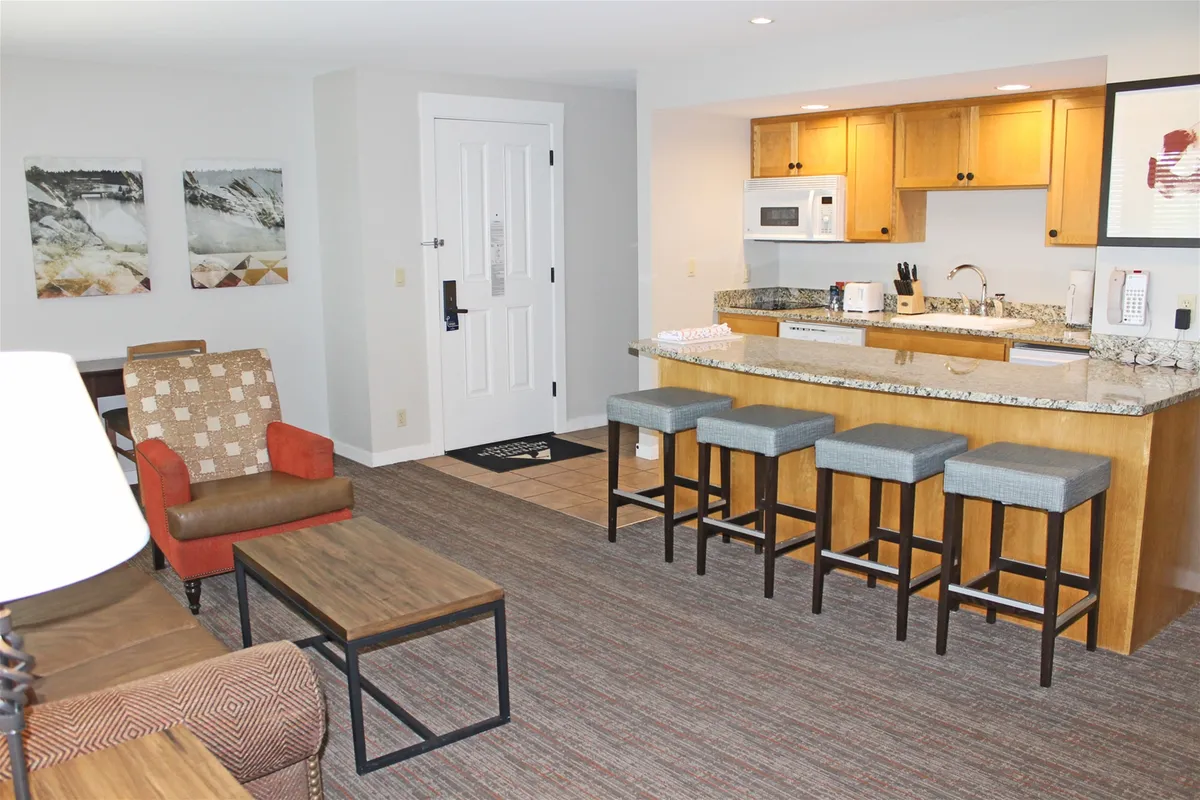 A stylish kitchen space with bar stools, living area seating, and artwork on the walls. The image showcases the open connection between kitchen and living, providing a glimpse of both cooking and entertaining areas.
