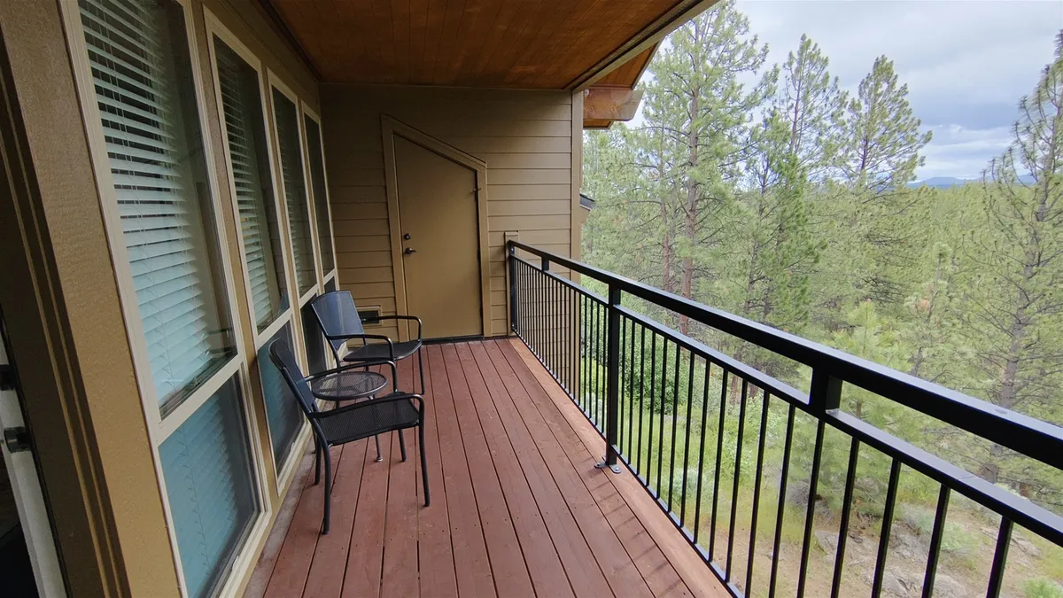A close-up of a private balcony with two black chairs and a wooden deck, looking out over lush greenery. The setup is intimate, showing just enough of the balcony to evoke a sense of privacy—perfect for quiet reflection or a romantic coffee for two, with a direct view into the trees.