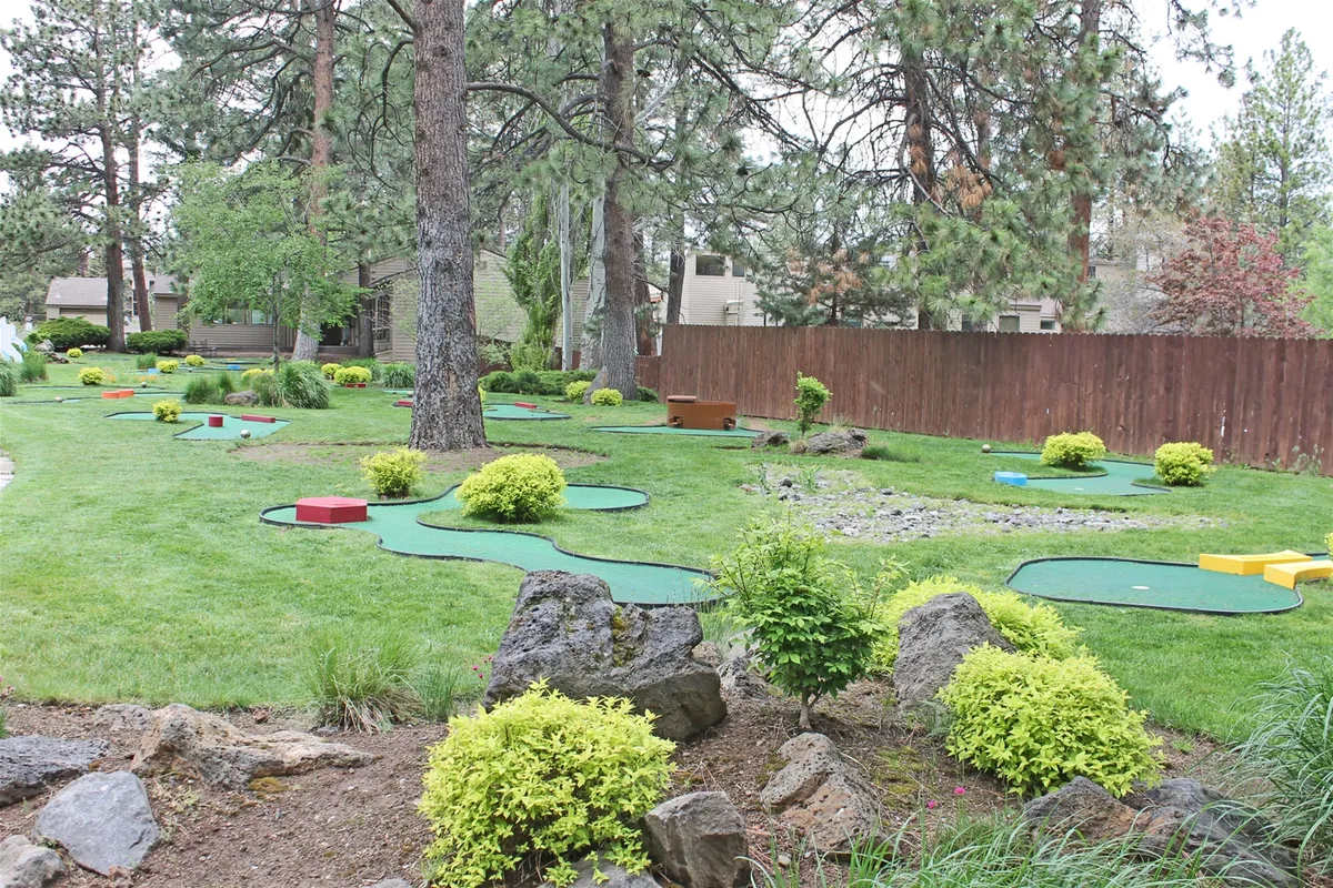 This vibrant scene depicts a miniature golf course set amid lush greenery, decorative rocks, and a wooden fence. It radiates energy and excitement, ideal for friendly family competition and enjoying the outdoors together.
