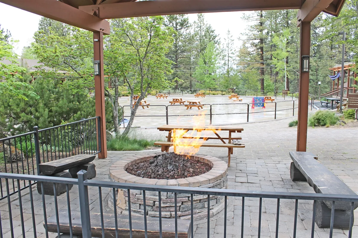 A cozy fire pit area surrounded by picnic tables and greenery, inviting guests to gather outdoors as the sun sets. The space offers a romantic spot for couples to enjoy quiet evenings or share stories under the stars.