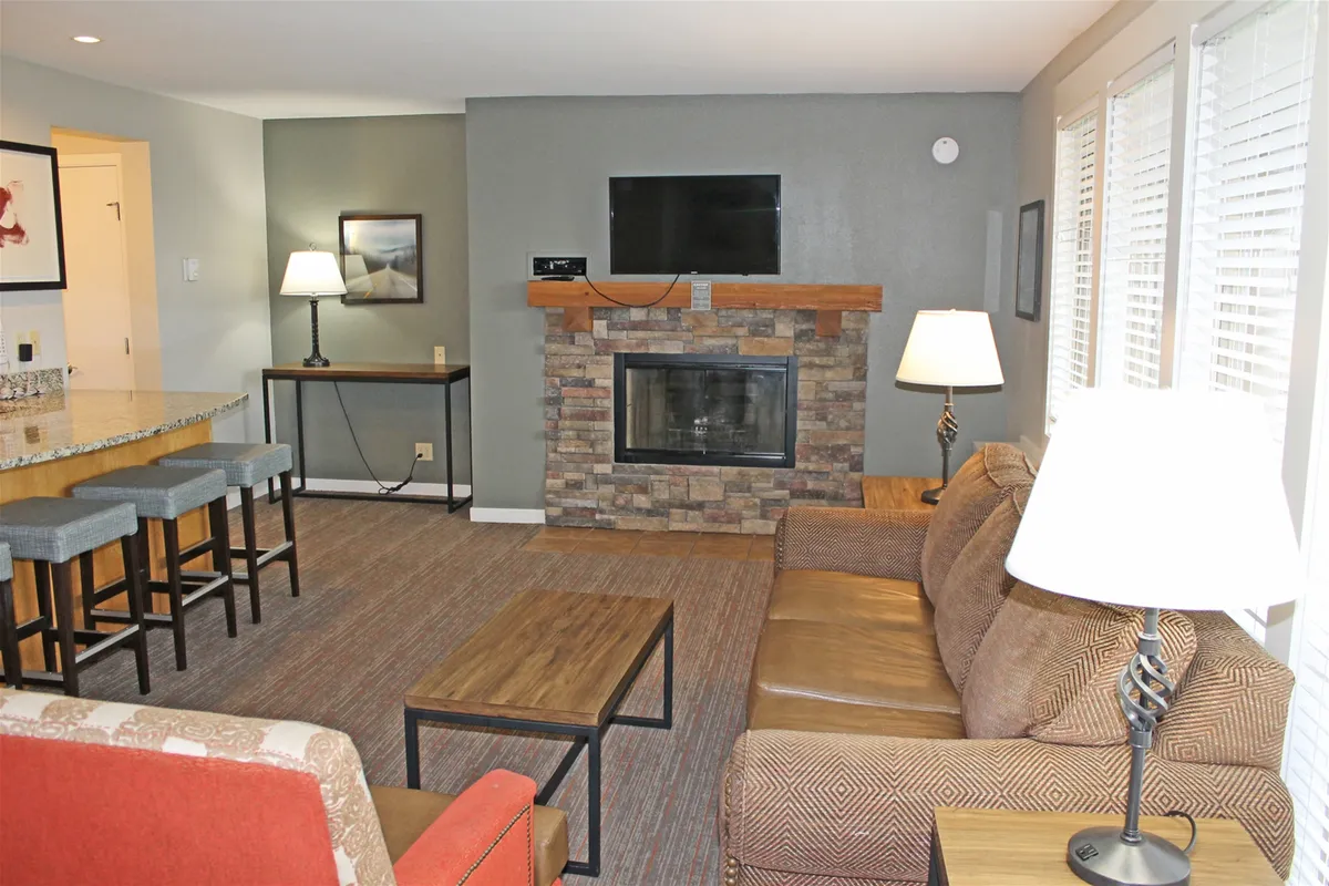 A cozy living area centered around a stone fireplace, with comfortable seating, a TV, and a bar counter. The ambiance is perfect for unwinding after adventure-filled days, socializing, or sharing drinks by the fire.