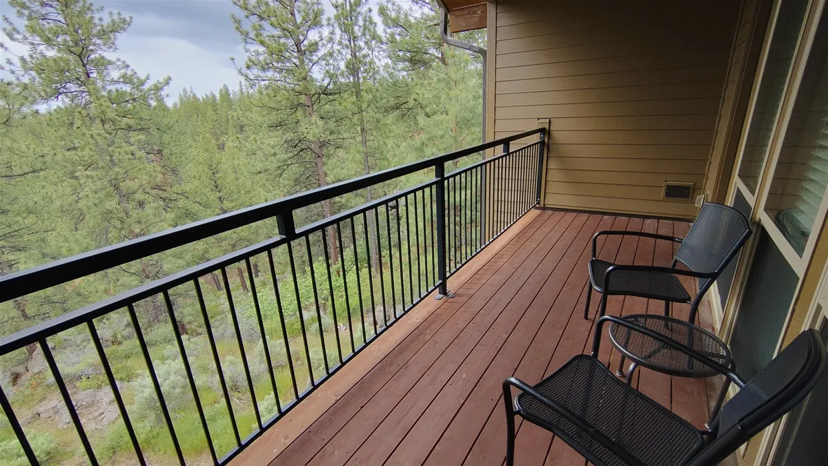A peaceful balcony scene with a wooden deck, two chairs, and a view of trees. The space exudes tranquility and invites guests to relax and soak in the mountain air, directly tying into the narrative of unwinding after a day of adventure.
