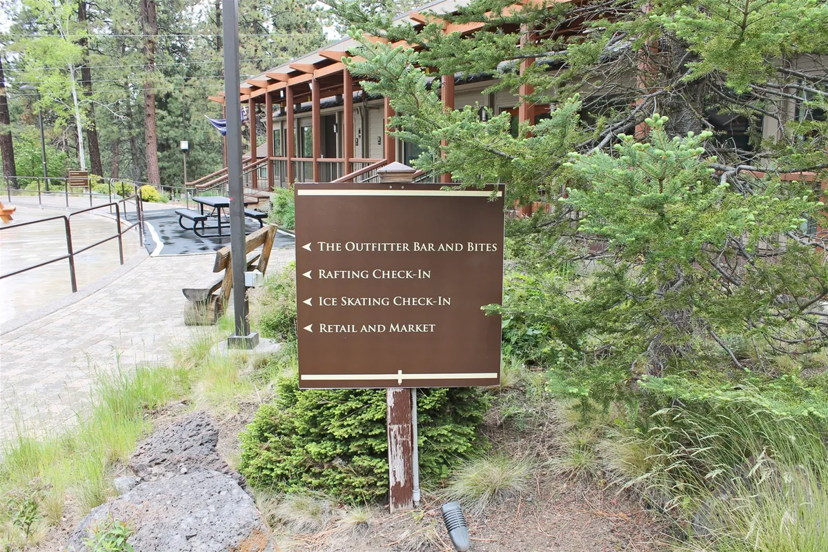 A colorful signpost points the way to a range of resort activities, surrounded by greenery and hinting at a building structure in the background. Activities like rafting, ice skating, shopping, and dining are indicated, suggesting a robust array of seasonal opportunities.