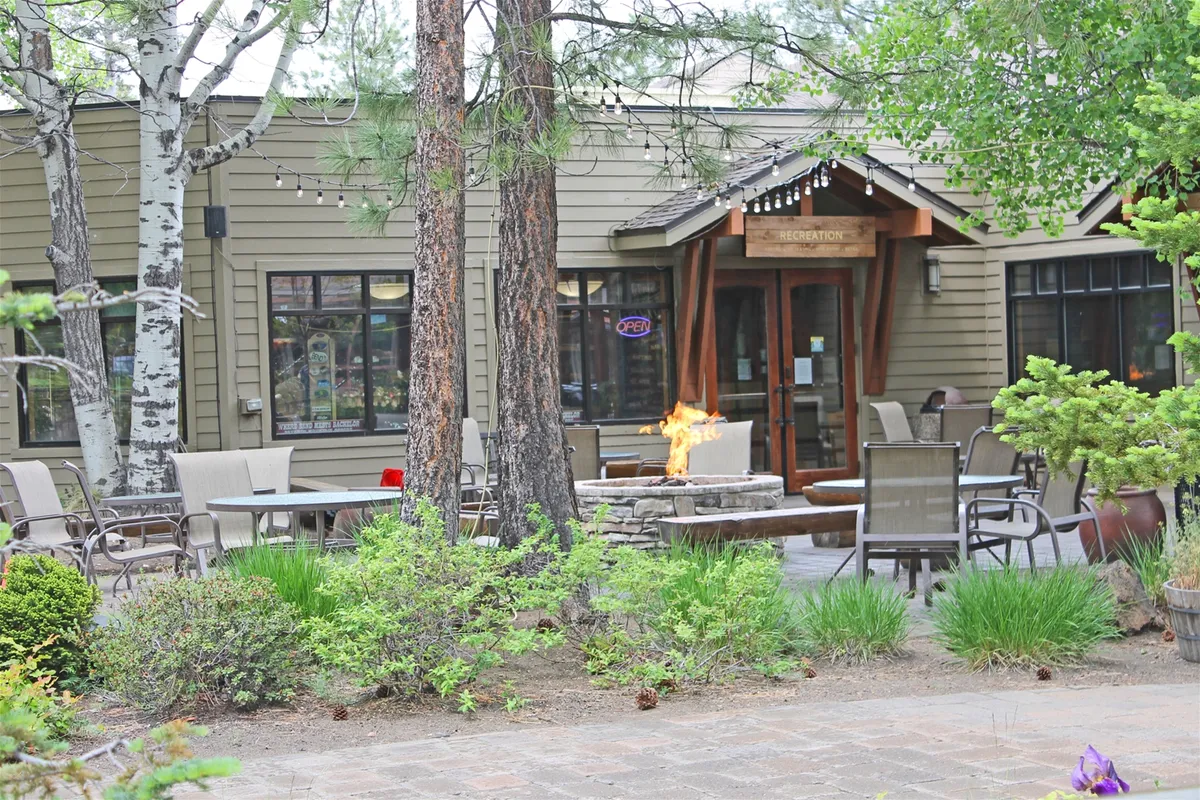 An exterior shot featuring a cozy fire pit with a welcoming seating area, the entrance to the building, and surrounding trees. The communal space suggests warmth, relaxation, and gathering after outdoor activities.