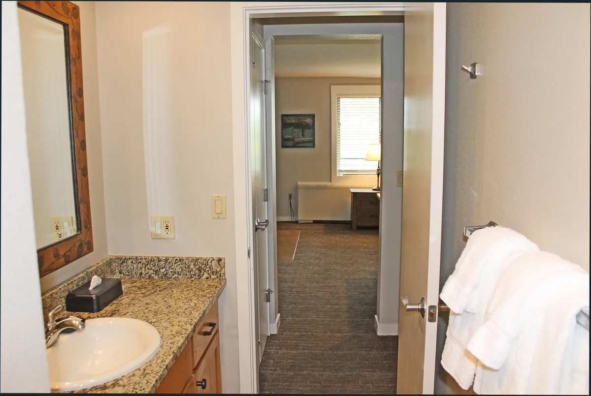 A well-appointed ensuite bathroom featuring a granite countertop, large mirror, soft towels, and a doorway that visibly connects to the bedroom. The setting is cozy and calm, suggesting private morning or evening routines.