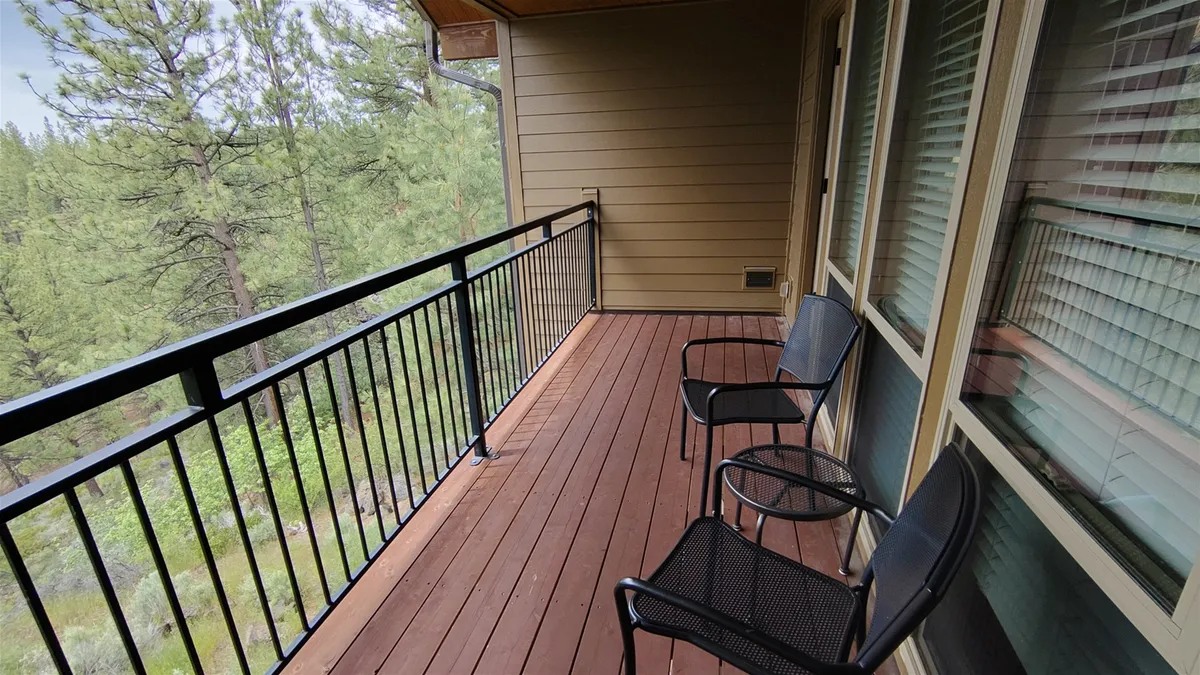 This image showcases an exterior balcony with a sturdy railing and inviting chairs, surrounded by lush greenery. The natural outdoor setting is tranquil and hints at a direct connection from the accommodations to the beautiful wintry outdoors, even though there is no visible snow.
